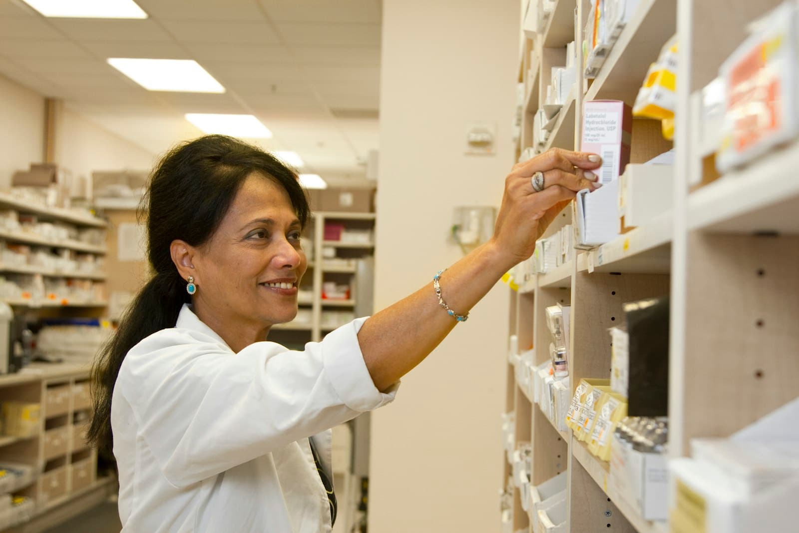 A pharmacist reaching for a medication on the shelf